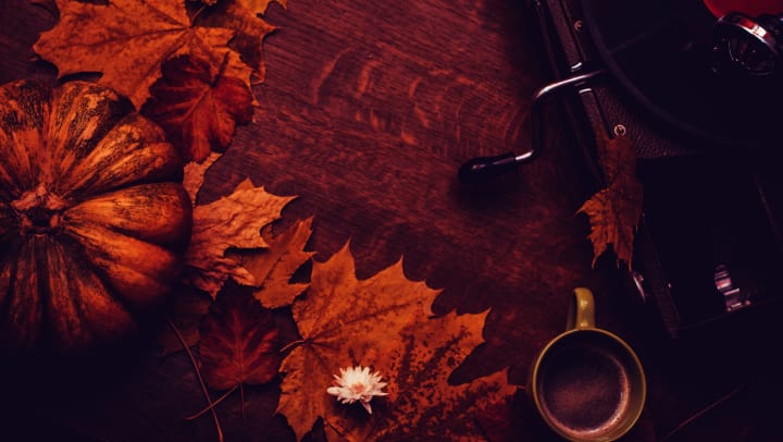 Aerial view of autumn leaves, an orange pumpkin, a green mug, and a vintage record player on a dark wooden table