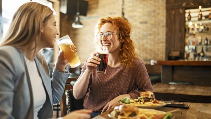 Two female friends smiling while eating dinner and drinking a beer | oldest restaurants in Savannah
