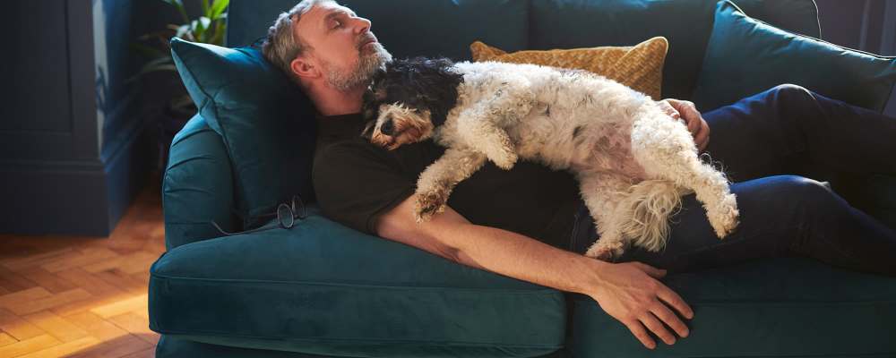 Man relaxing on sofa with his dog lying on top of him at The Miller in Tacoma, Washington