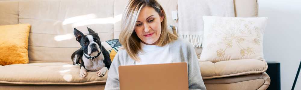A woman using her laptop with her small dog near her at Avalon in Davis, California