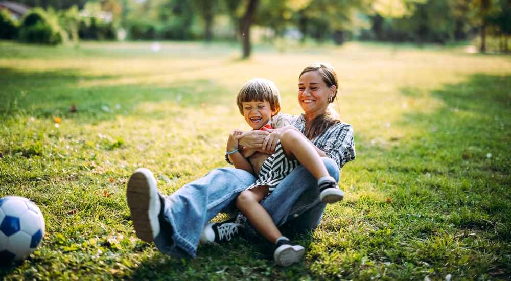 Woman playing with young boy in grassy park near Eban Village Apartments in Dallas, Texas