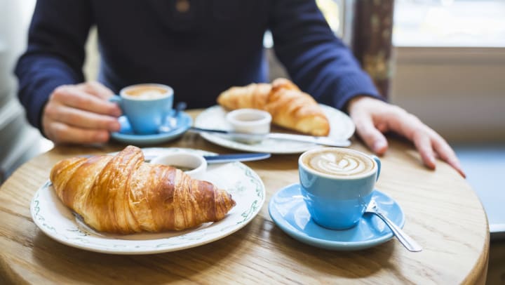 Man sitting at a small round table with two cups of coffee and two croissants | breakfast in Odessa