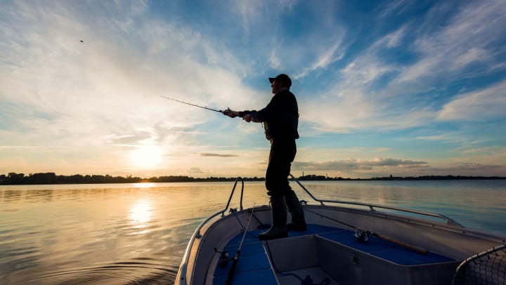 Angler standing atop a boat casts a fishing line into the water