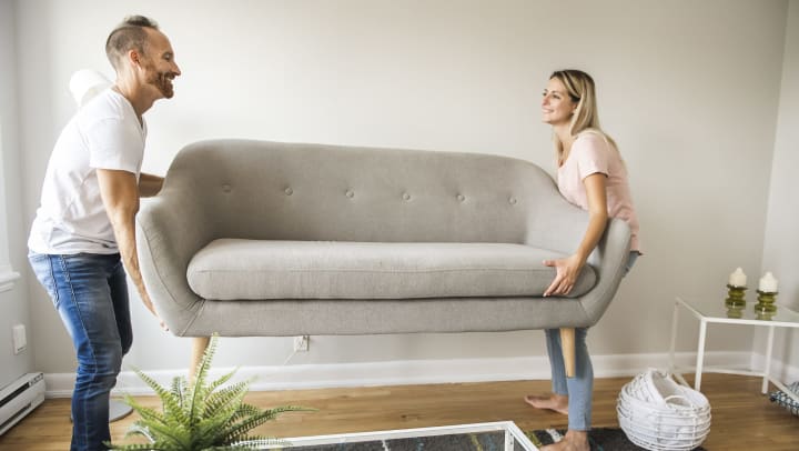 A smiling man and woman placing a sofa in their living room