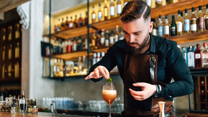 Bartender standing behind a bar, garnishing a cocktail.