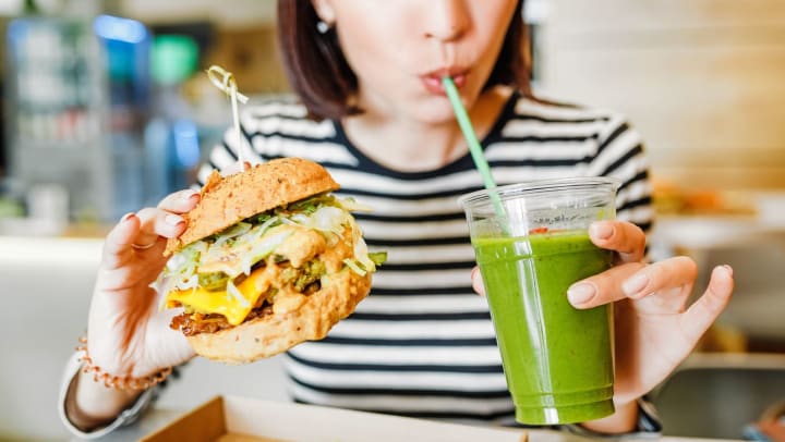 A young woman drinks a green smoothie and eats a burger in a vegan fast food restaurant | vegan restaurants in Pompano Beach