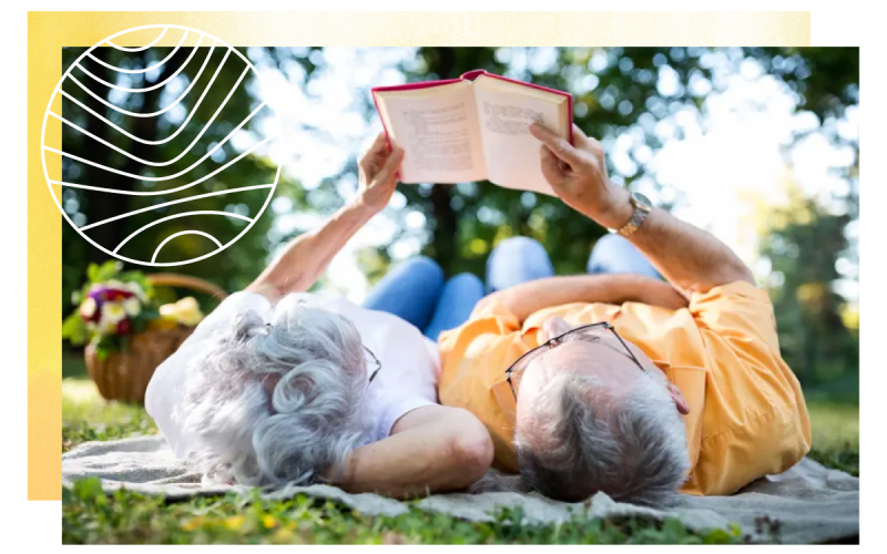Resident couple reading a book while laying out on the grass at a Chancellor Gardens community