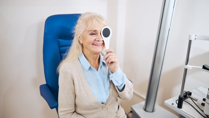 A smiling older woman covers one eye during a vision test.