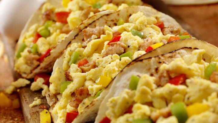 Three tacos filled with eggs, meat, and red, yellow, and green bell peppers.