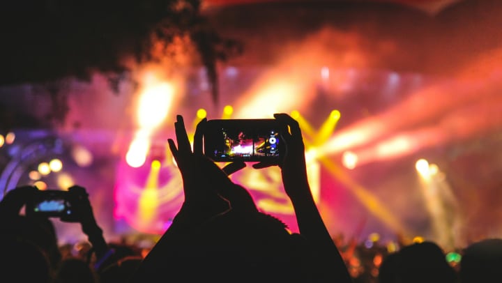 Person holding smartphone taking a video of a concert near stage with lights during nighttime