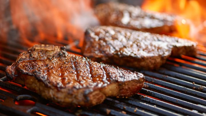Closeup of steaks grilling over flame 