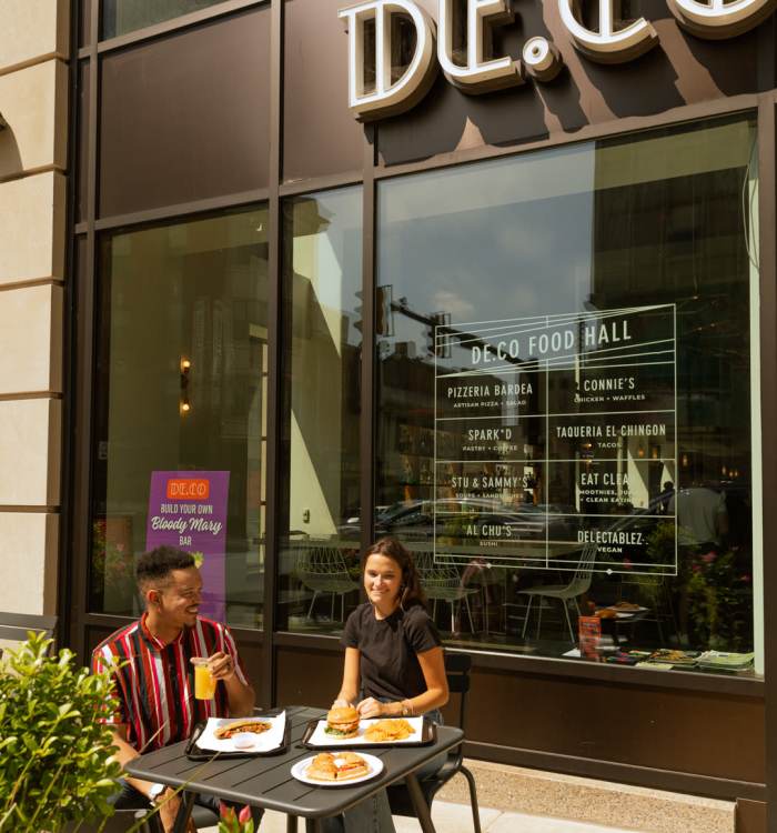A couple eating outside Deco Food hall near The Residences at Christina Landing in Wilmington, Delaware