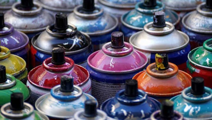 A closeup of collected spray paint cans of various colors, all used by a street artist