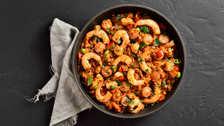 Top view of creole style jambalaya with prawn, chicken, smoked sausages and vegetables in frying pan over black stone background | Jambalaya Near The Woodlands