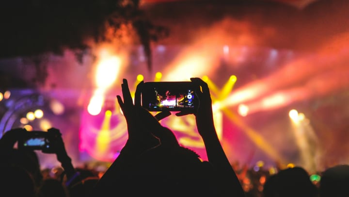 Person holding smartphone taking a video of a concert near stage with lights during nighttime