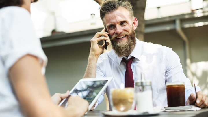 A man with a beard and tie having a phone conversation.