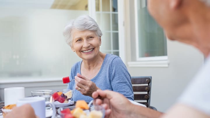 Senior woman smiling looking at a senior man while eating fruit.