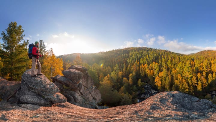 Man standing atop a boulder against a backdrop of mountains covered in bright fall foliage