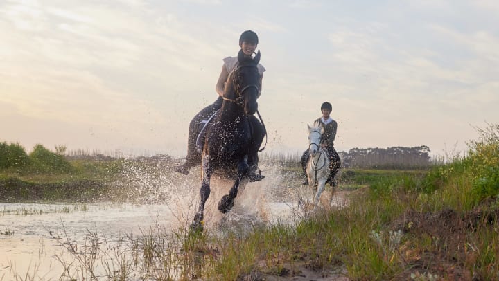 Two horses and riders galloping through water