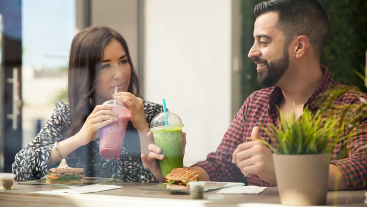 Two people drinking smoothies and eating sandwiches