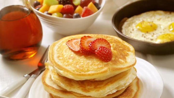 table full of breakfast food, including pancakes, syrup, fruit, sausage, and orange juice | breakfast restaurants in Jacksonville