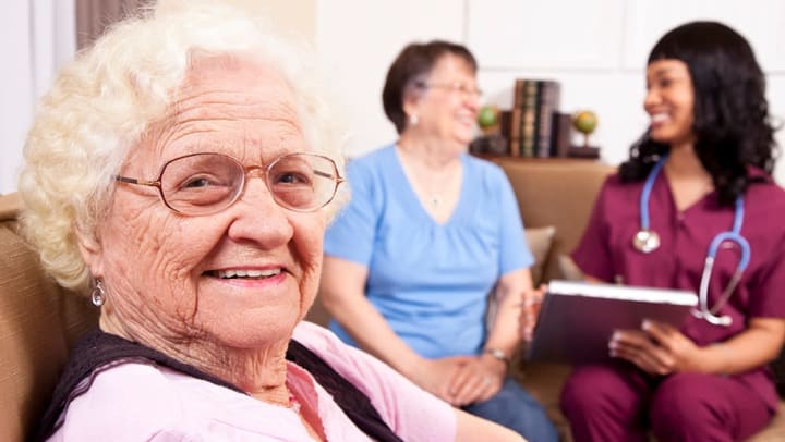 Female senior smiling while a caregiver is meeting with a resident in the background.