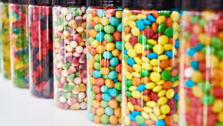Brightly colored candies stored in clear glass jars on a shelf.