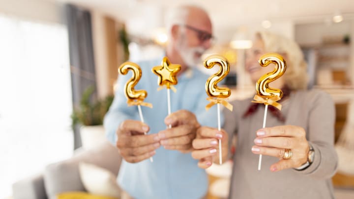 Cheerful senior couple holding golden balloons shaped as numbers 2022.
