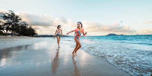 Two young girls joyfully running along the sandy beach near Bayside Villas Apartment Homes in South Pasadena, Florida