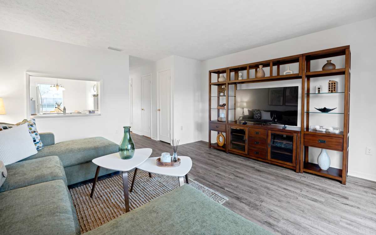 Living room with wood-style flooring, sectional sofa, and stylish entertainment unit at Carlton Arms North in Tampa, Florida