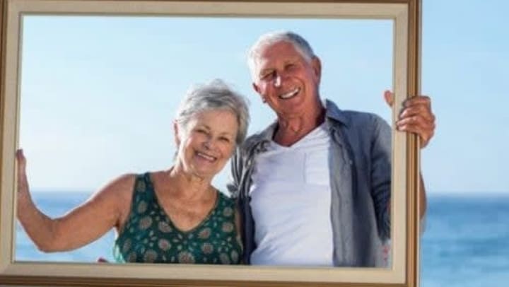 A couple holding a picture frame around them by the waterfront