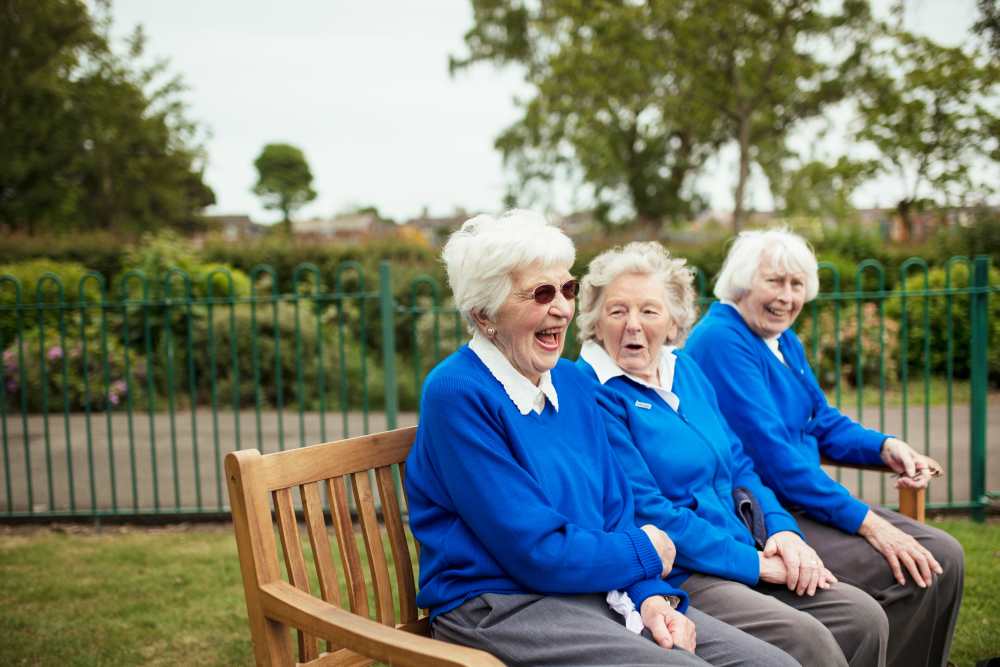 Three senior citizens sitting on a bench together and laughing