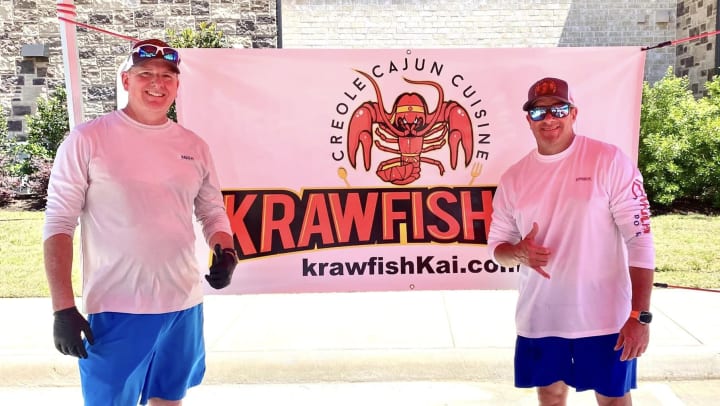 Two men standing with banner that says Krawfish which is their company name