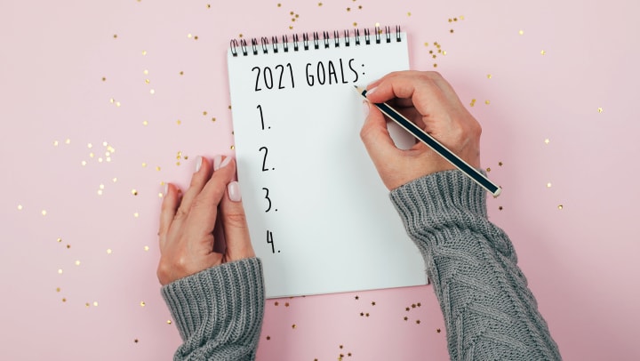 Overview pic of hands writing “2021 Goals” on notebook paper.