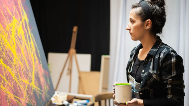 An artist holds a can of green paint in her hands and looks toward a canvas