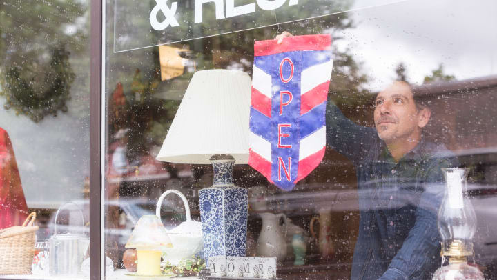 A man flipping the open sign in the window of a Frisco resale shop.