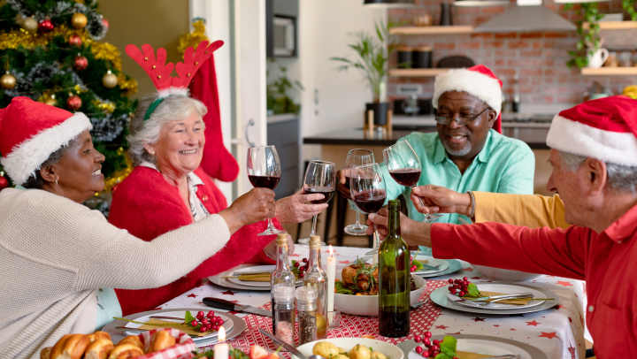 Seniors sitting around a table cheering and wearing holiday hats.