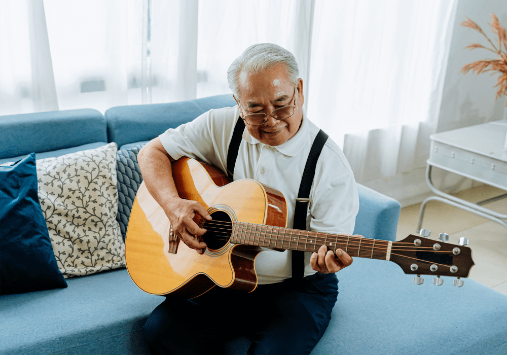 Resident sitting on a couch and playing an acoustic guitar at Sunstone Village in Denton, Texas