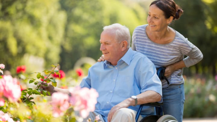 a woman carring an older man in a wheelchair