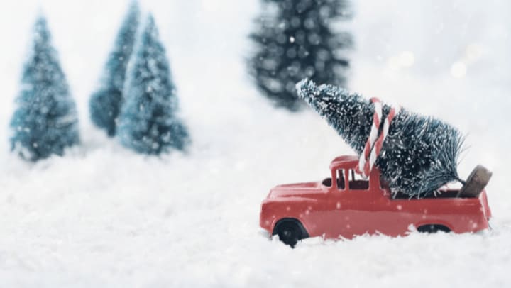 Small red truck carrying a Christmas tree through snowy winter scene, representing holiday storage planning and secure self storage options in Portland Oregon
