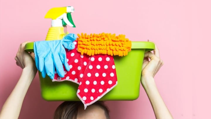A woman holds up a bucket of cleaning supplies.