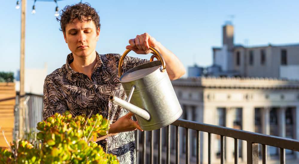 Resident is watering plants on an urban garden terrace at The Lofts at 305 in Bryan, Texas