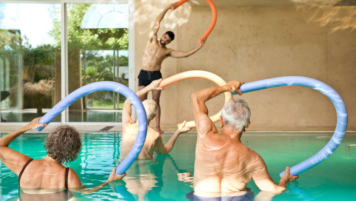 Three seniors standing in pool using noodles to exercise