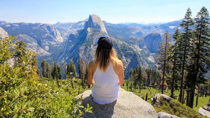 Woman sitting on a rock in nature overlooking Half Dome in Yosemite National Park
