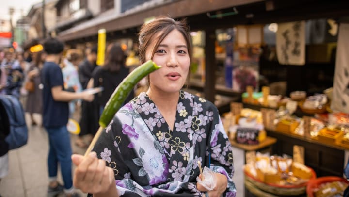 Woman on street eating a pickle on a stick.