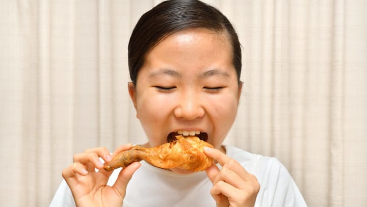 Woman eating a fried chicken drumstick.