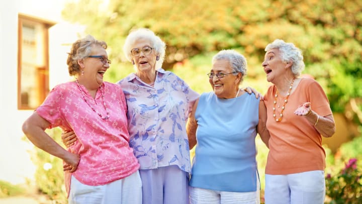 Four elderly women outside standing beside each other smiling.