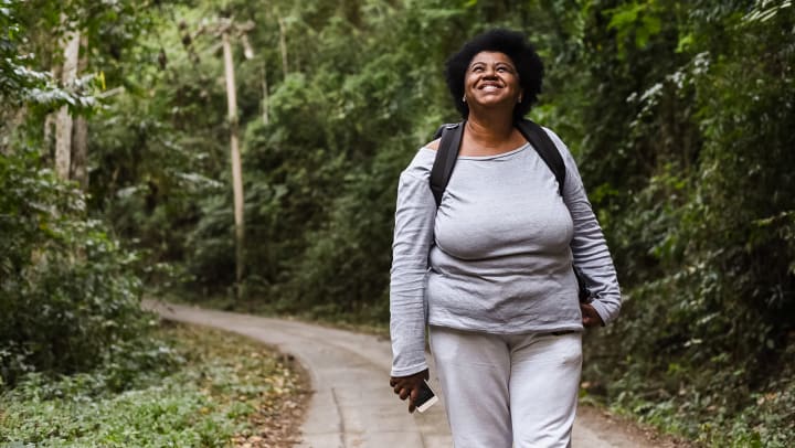 Woman in athletic wear and a backpack standing on an outdoor trail, looking up and smiling. 