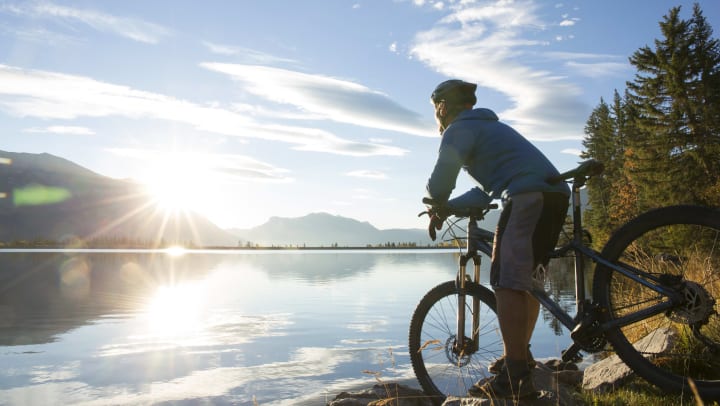 Mountain biker relaxes by lakeshore at sunrise.