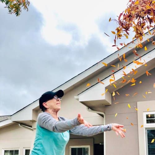 A resident tossing leaves outside at Oxford Glen Memory Care at Sachse in Sachse, Texas